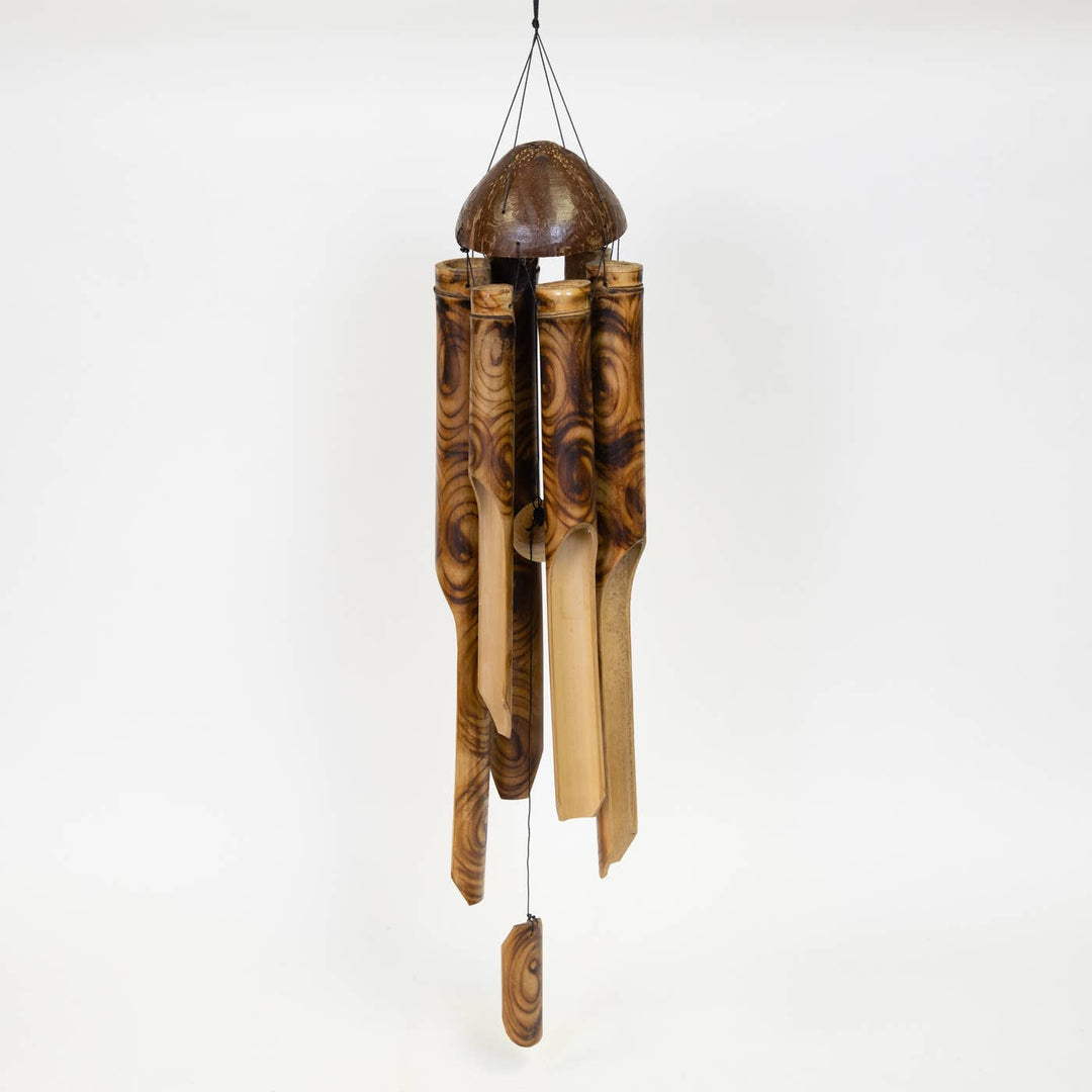 Handcrafted bamboo wind chime with coconut top hanging in a garden setting.