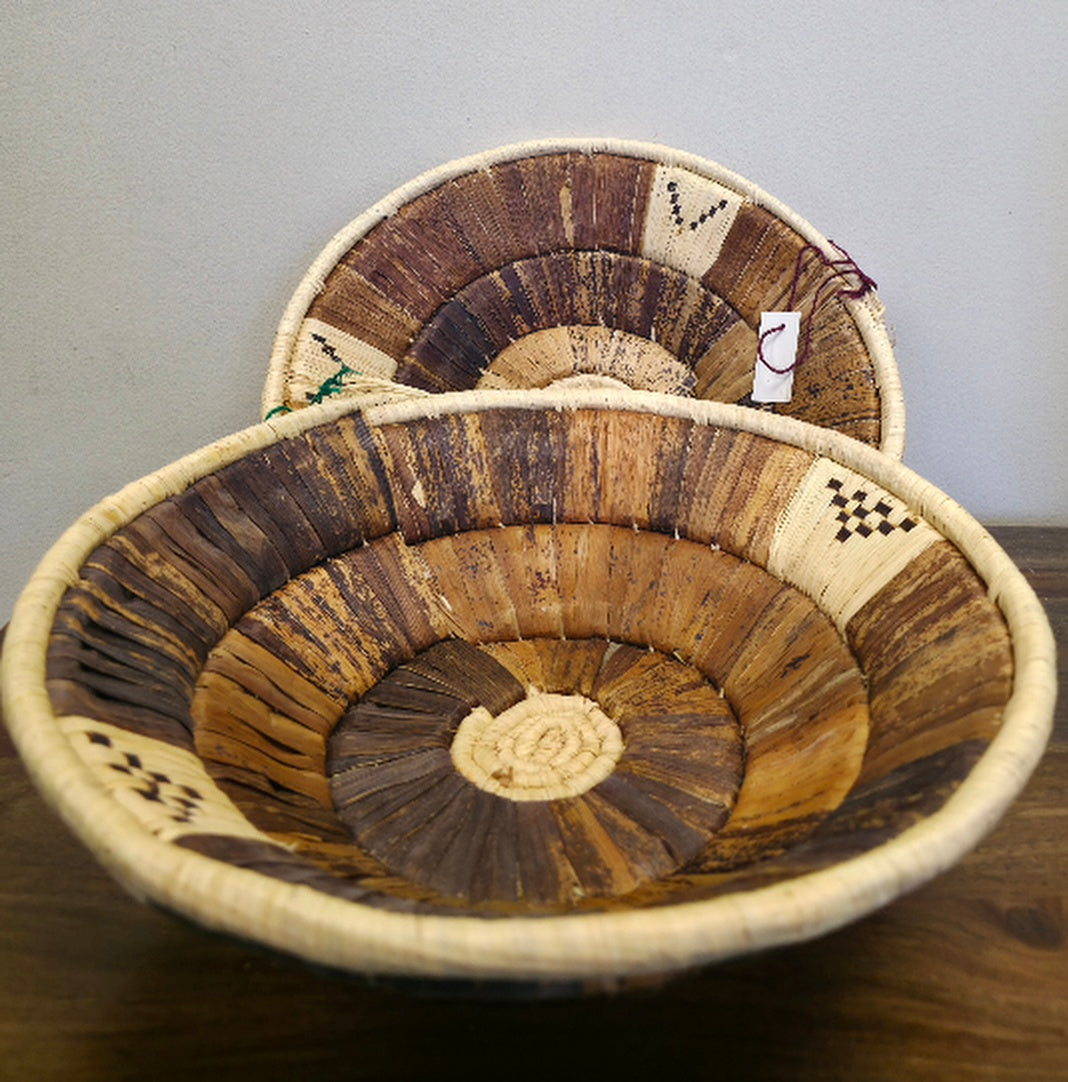 A round handwoven wall basket with banana leaf, made from raffia palm and banana leaves, intended for indoor use as wall art or storage.