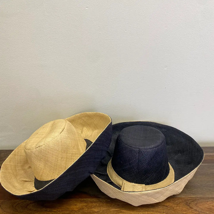 Two hats, one beige and one black, stacked on a wooden surface with a plain background. Great hat for parties, beach and the park.