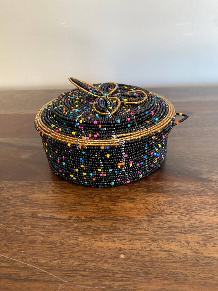 Fair trade beaded container on wooden shelf with natural light.