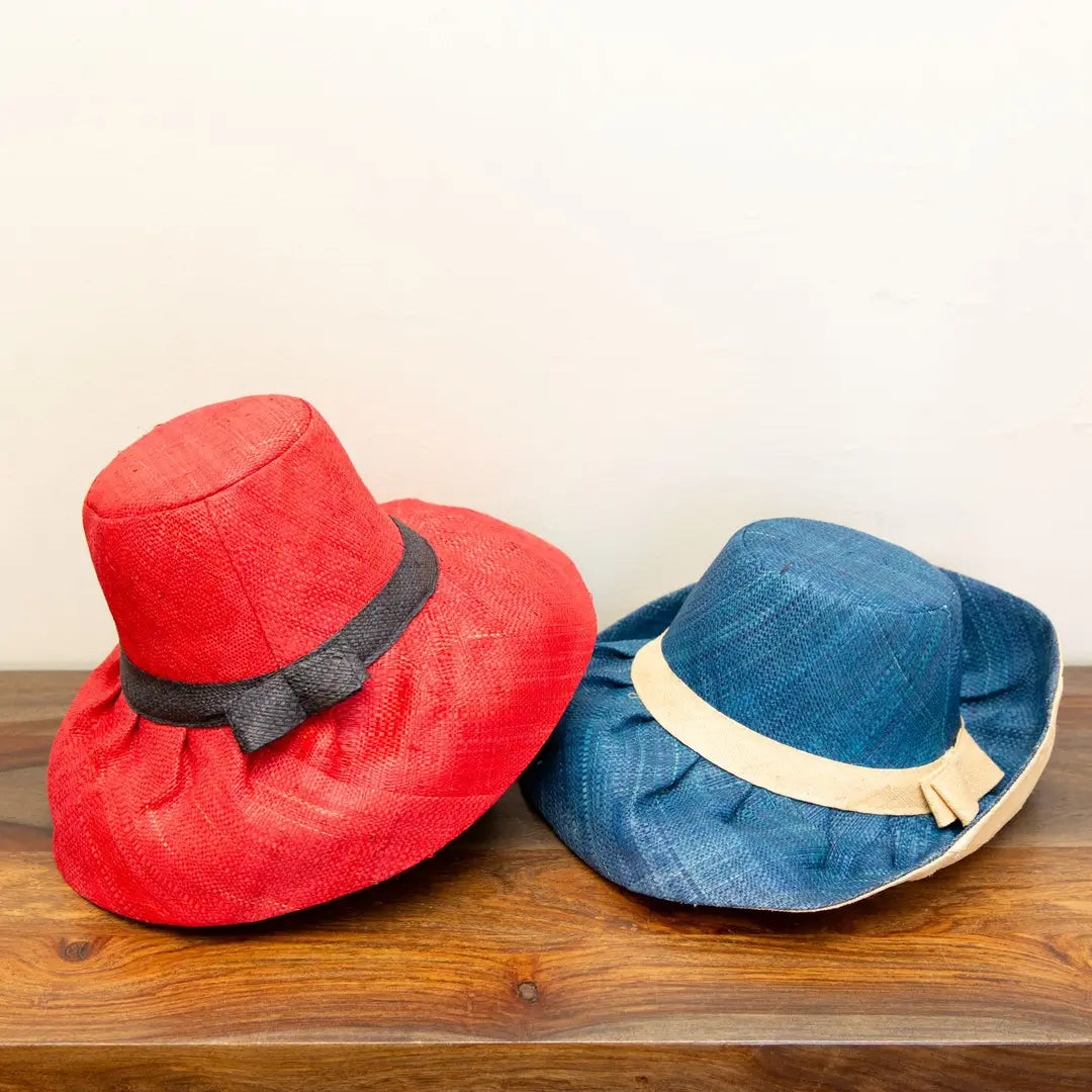 Red and blue hats with decorative bands on a wooden surface. Hats are sustainable and fair trade.