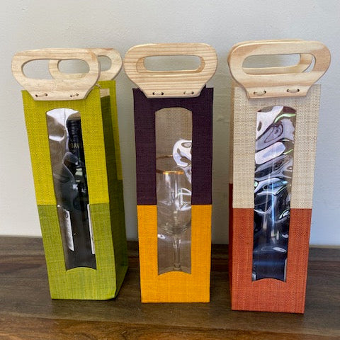 Three colorful wine bottle gift bags with handles on a wooden surface.