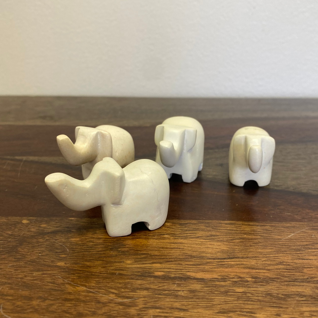 Four white soapstone elephant figurines on a wooden surface with a plain background.