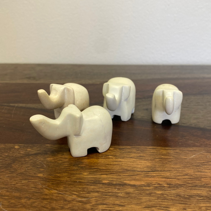 Four white soapstone elephant figurines on a wooden surface with a plain background.
