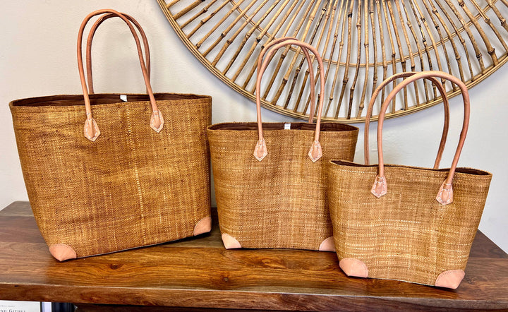 Fair trade solid color raffia handbag with leather handles and drawstring top.