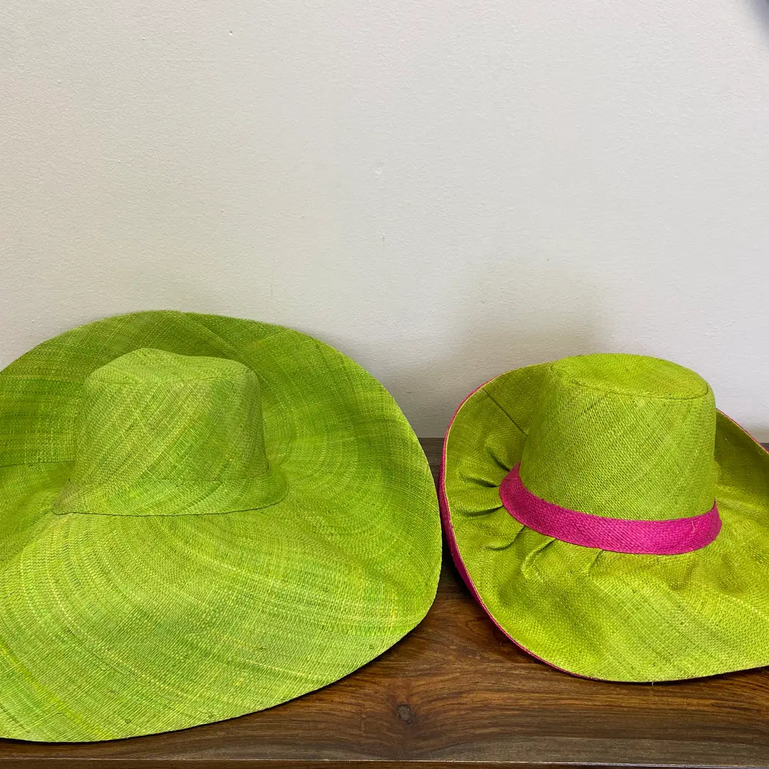 Two green sun hats, one with a hot pink band, on a wooden surface with a white background.