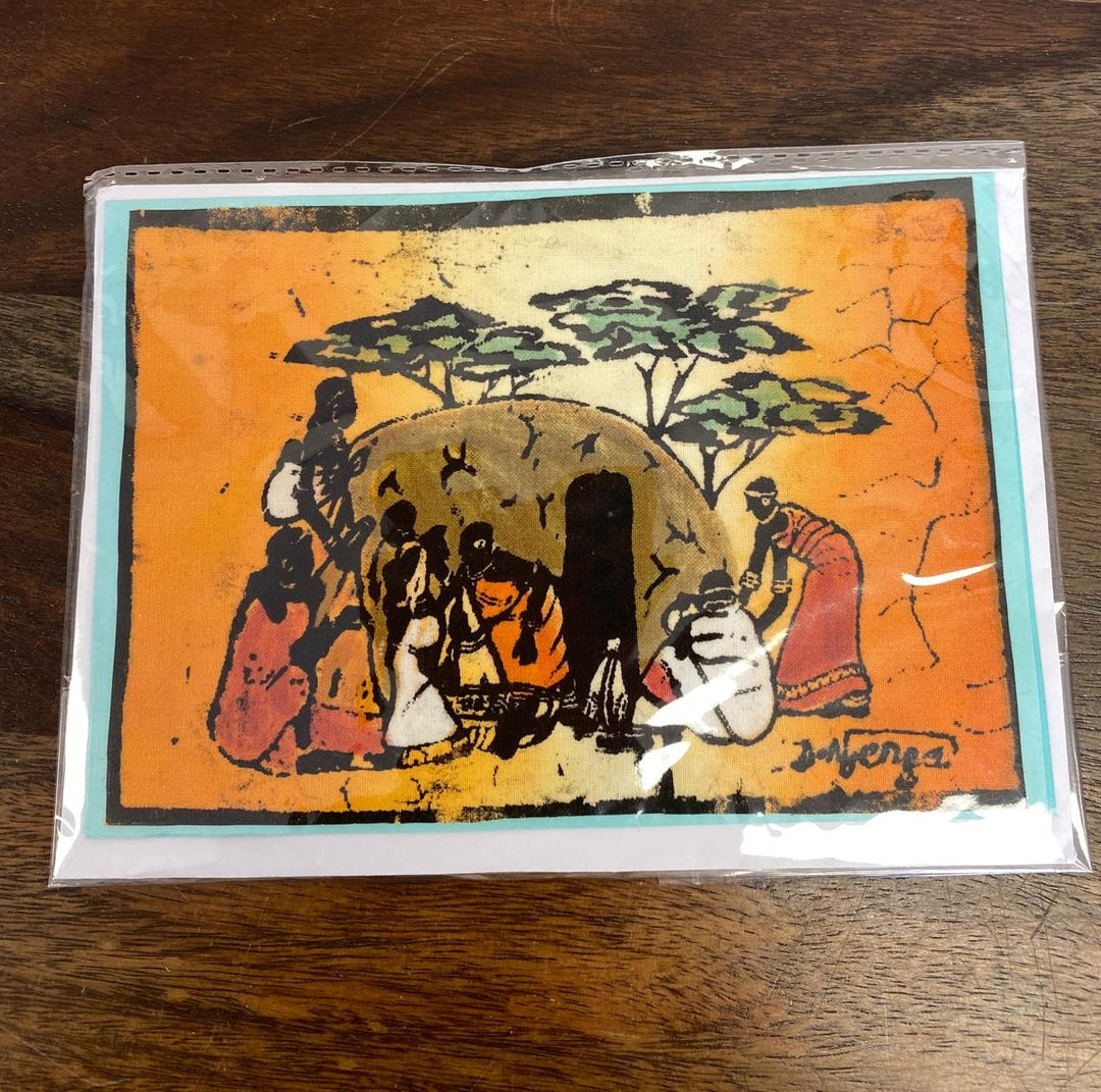 Decorative greeting card with a colorful illustration of Masai people around a fire on an orange background, placed on a wooden surface. Fair trade.