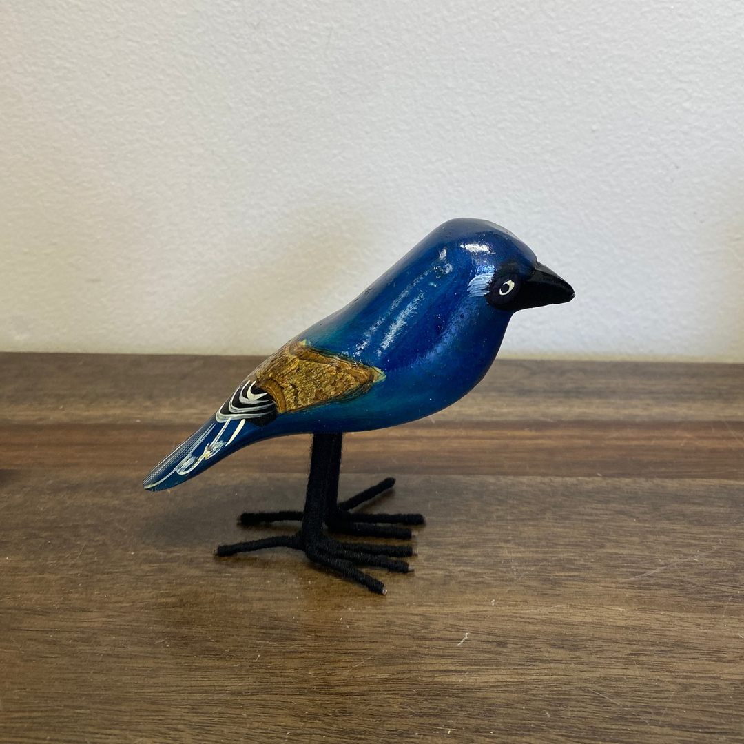 Front view of fair trade hand carved wooden bluebird ornament, painted in vibrant blue with detailed wings, standing on carved base.