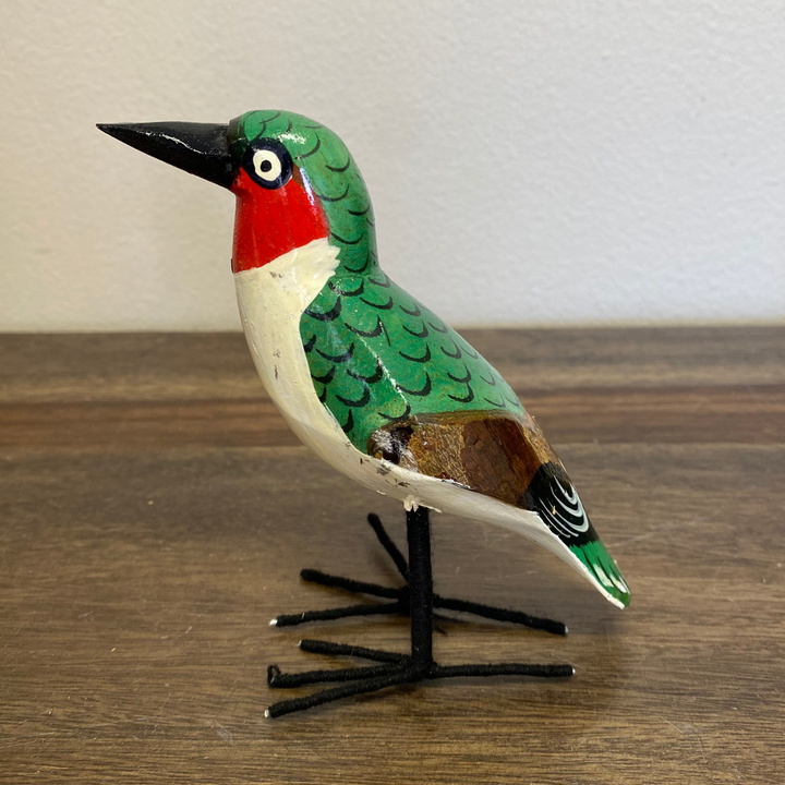 Front view of fair trade wooden hummingbird ornament, hand painted green with delicate carved details, standing upright.