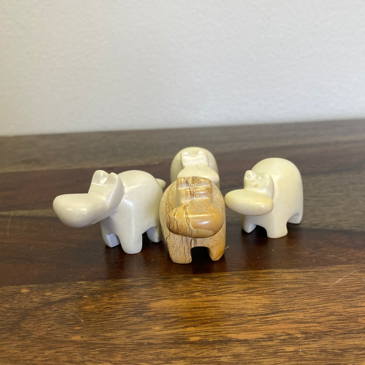 Three ivory colored small soapstone hippopotamus figurines on a wooden surface with a plain background.