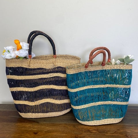 Two woven baskets, one with black and beige stripes and a black leather handle and the other with blue and beige stripes with a brown leather handle, on a wooden surface.