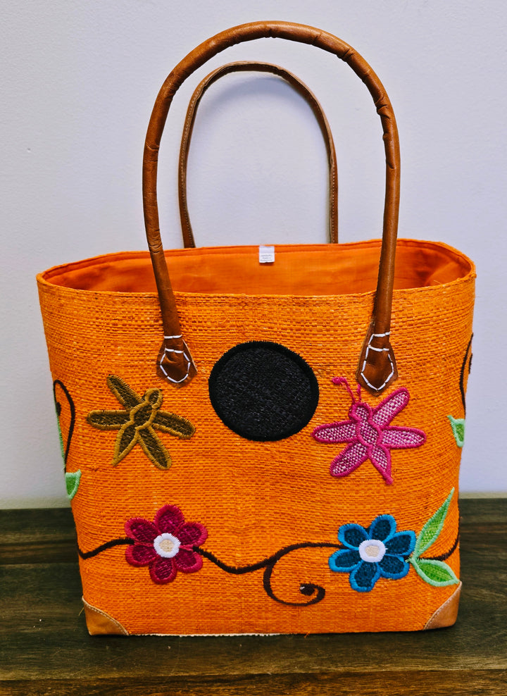 Artisan-crafted raffia purse featuring vibrant flower patterns and palm leaf weave.