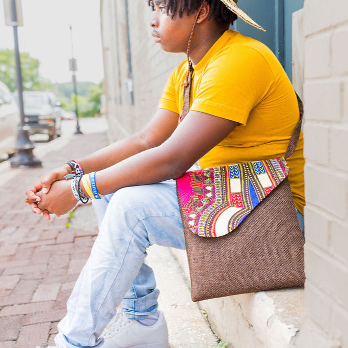 Person sitting on a sidewalk holding a colorful, fair-trade, patterned bag that works as a great, medium sized crossbody bag.