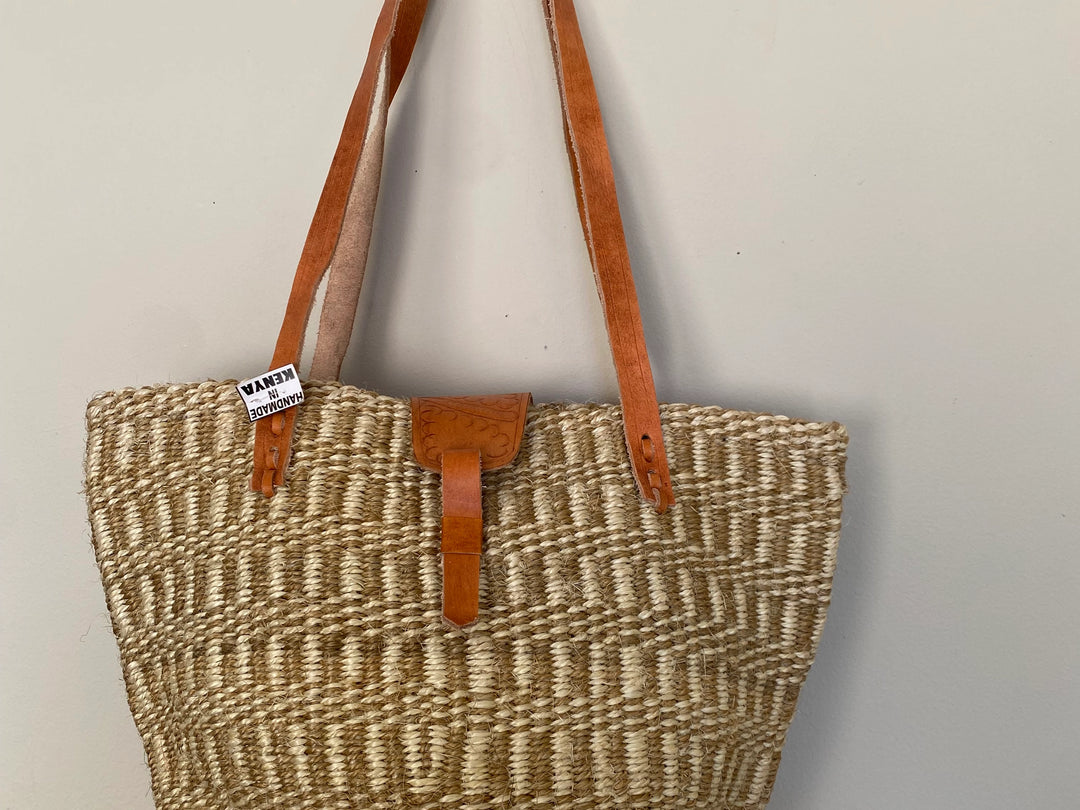 Woven bag with brown leather straps on a light gray background