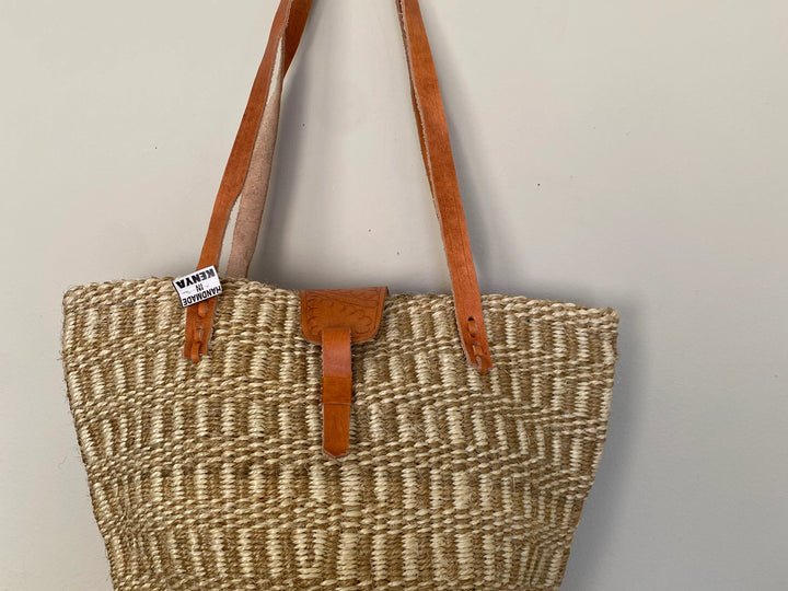 Woven bag with brown leather straps on a light gray background