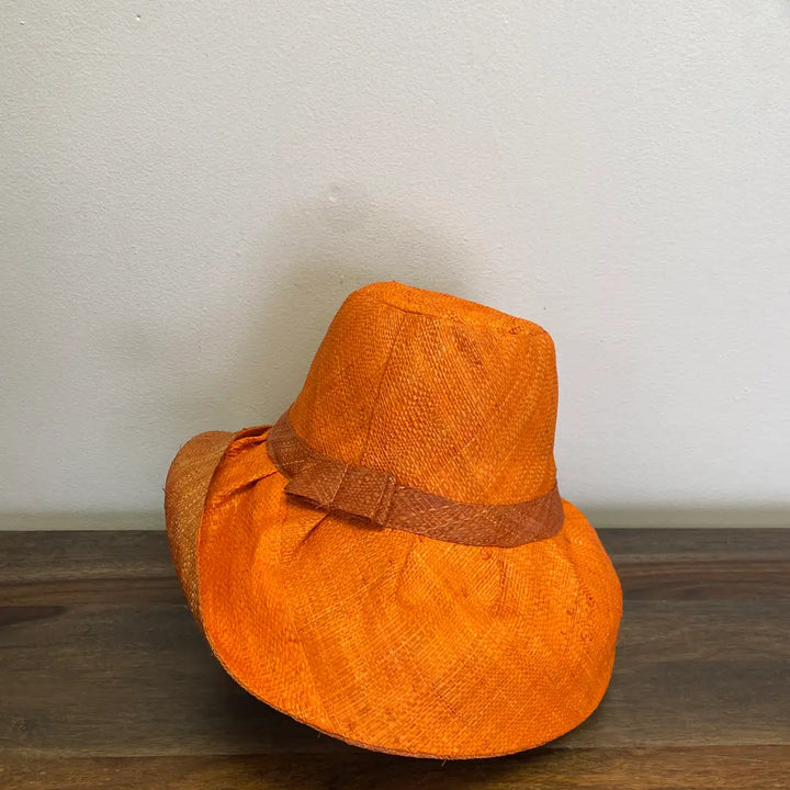 Orange woven hat with a brown band on a wooden surface. Great for the summer.