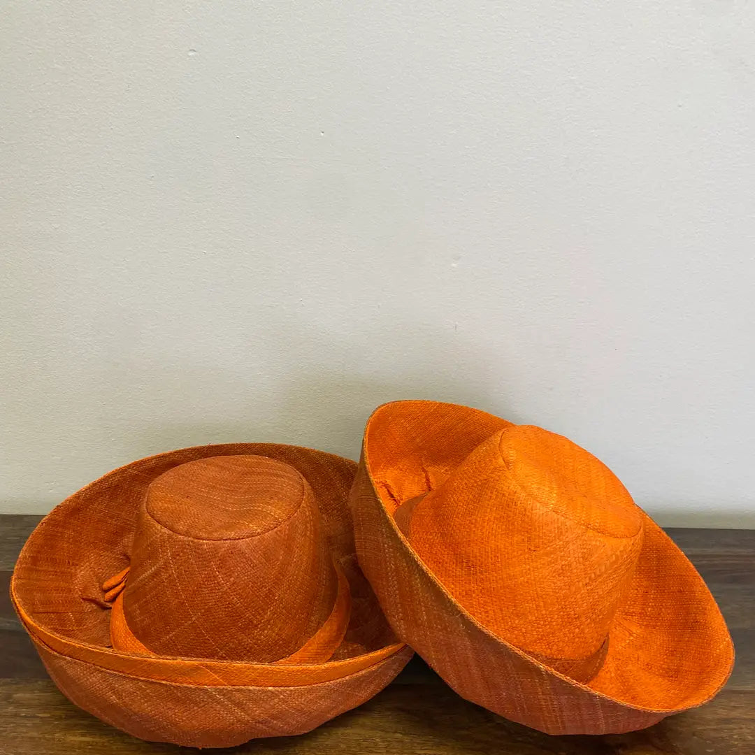 Two orange hats on a wooden surface with a plain background