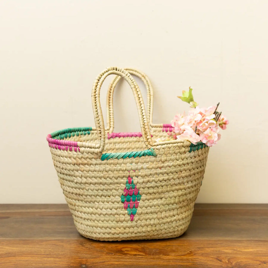 Woven basket with colorful handles and floral decoration on a wooden surface.