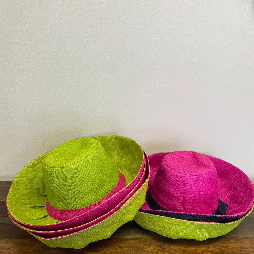 Two colorful hats, one green and one pink, on a wooden surface with a white background.