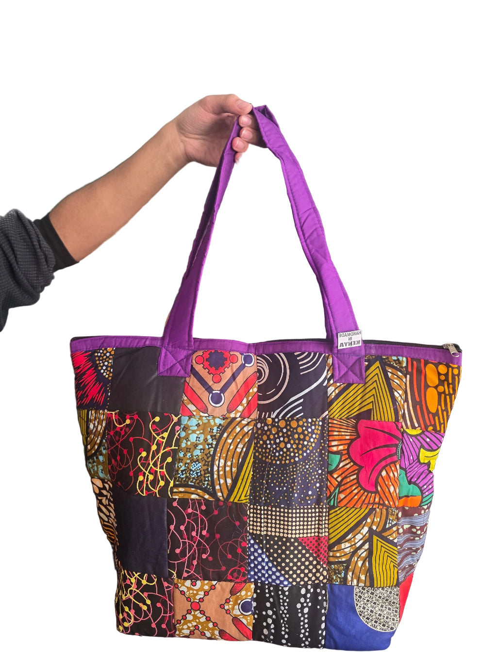 Colorful patterned bag with a purple strap held by a person against a green wall.