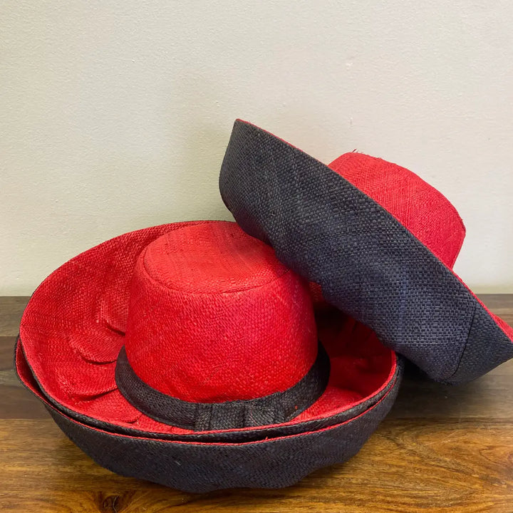 Red and black hats stacked on a wooden surface with a neutral background.
