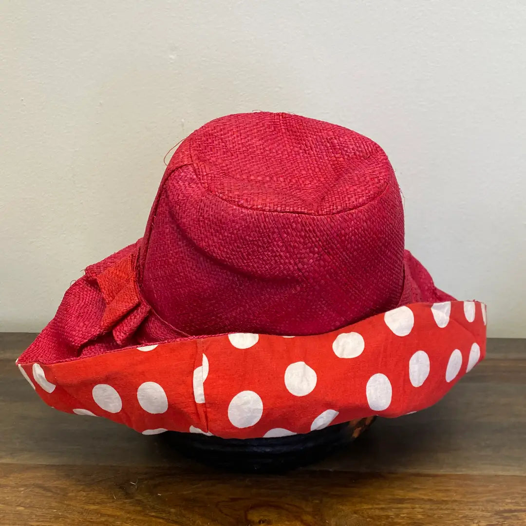 Red sun hat with a white polka dot lining on a wooden surface. Great for the beach.