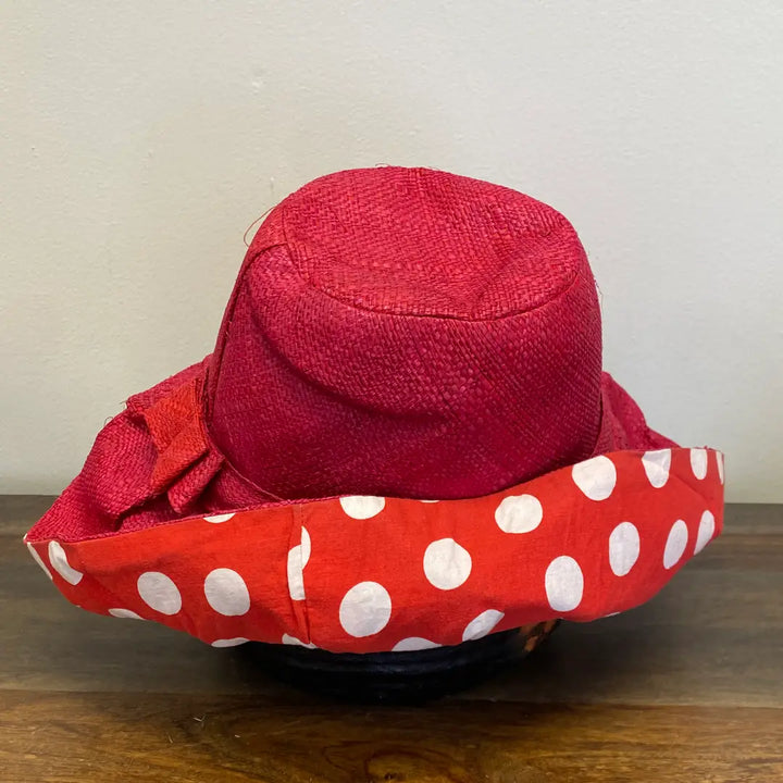 Red sun hat with a white polka dot lining on a wooden surface. Great for the beach.