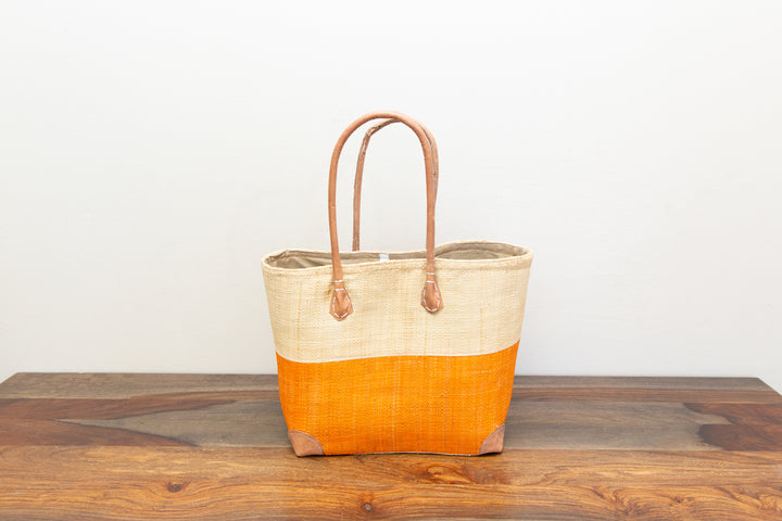 Two-tone fair trade raffia handbag with leather handles and drawstring top.