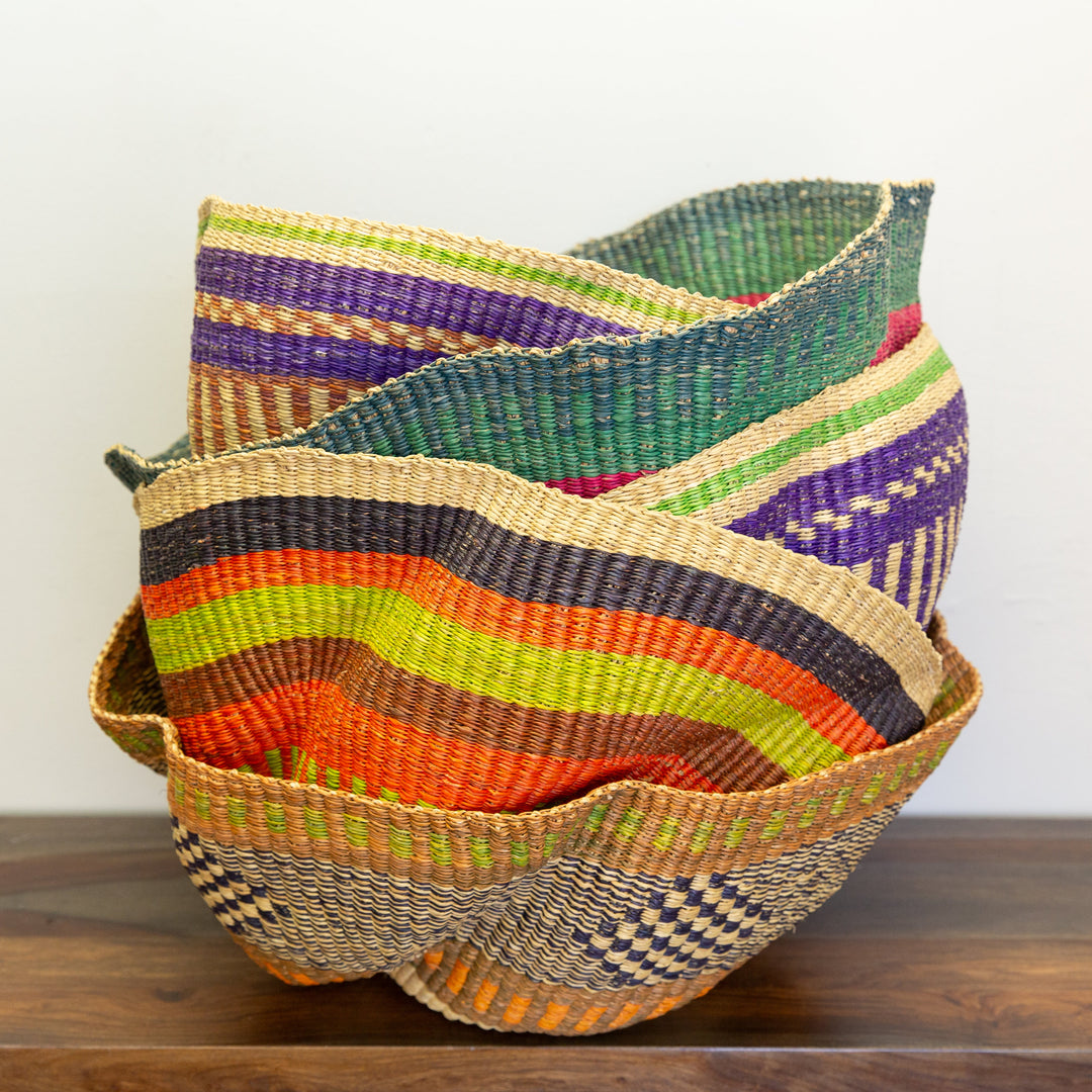A handwoven Bolga storage basket with a wavy pattern and a leather handle, featuring assorted colors.