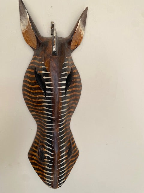 A hand-carved and hand-painted bamboo mask of a zebra's head with a hanger attached, featuring brown and black stripes.