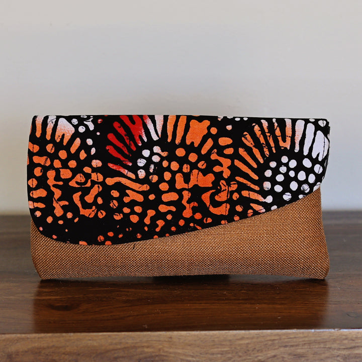 Multicolor African print clutch purse with batik pattern in orange, white, red, and black. Clutch has a structured fabric base.
