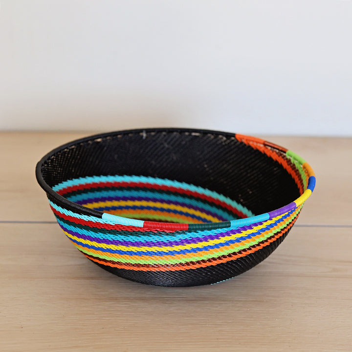 Black Rainbow Zulu Bowl handwoven in South Africa with colorful diagonal rainbow stripes on a black woven base.