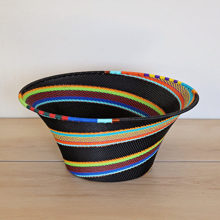 Black Rainbow Zulu Large Flared Bowl handwoven in South Africa with colorful diagonal rainbow stripes on a black woven base.