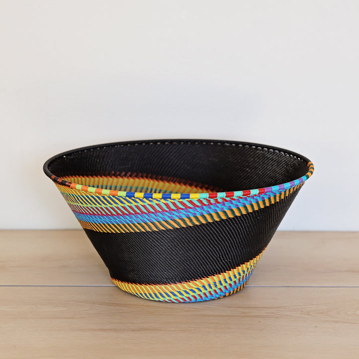 Black Rainbow Zulu Large Funnel Bowl handwoven in South Africa with colorful diagonal rainbow stripes on a black woven base.