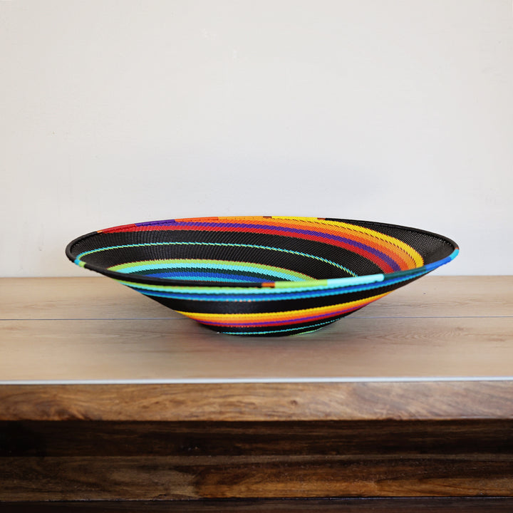 Black Rainbow Zulu Large Shallow Basket handwoven in South Africa with colorful diagonal rainbow stripes on a black woven base.