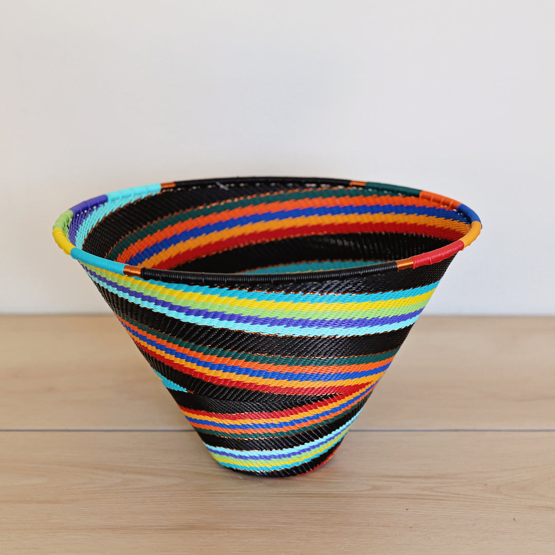 Black Rainbow Zulu Medium Deep Funnel Bowl handwoven in South Africa with colorful diagonal rainbow stripes on a black woven base.