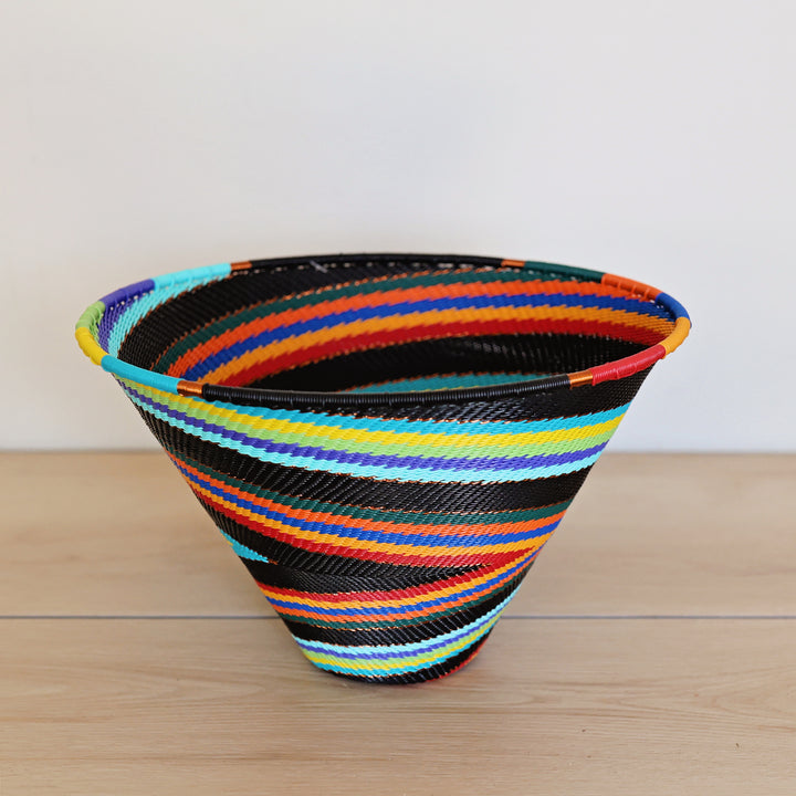 Black Rainbow Zulu Medium Deep Funnel Bowl handwoven in South Africa with colorful diagonal rainbow stripes on a black woven base.