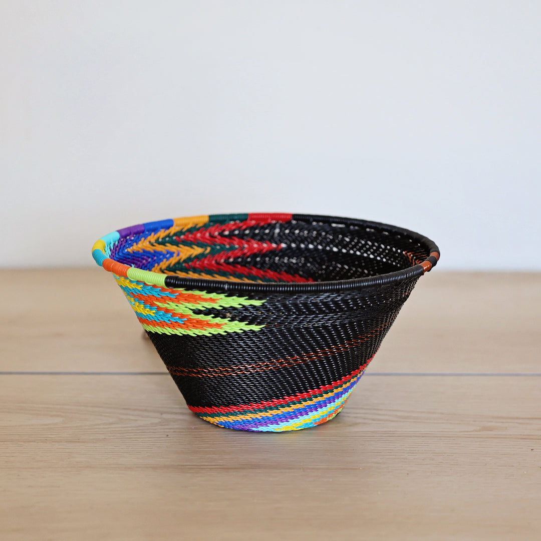 Black Rainbow Zulu Small Funnel Bowl handwoven in South Africa with colorful diagonal rainbow stripes on a black woven base.