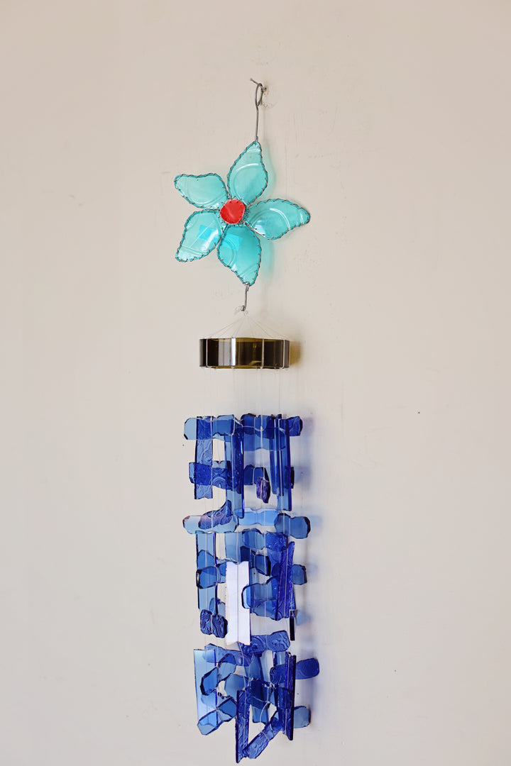 Decorative wind chime with blue and turquoise flower and blue rectangular design on a beige background