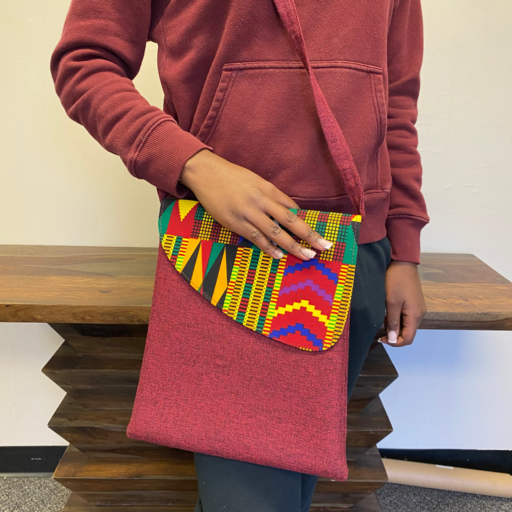 Person holding a red African patterned bag with a colorful flap.