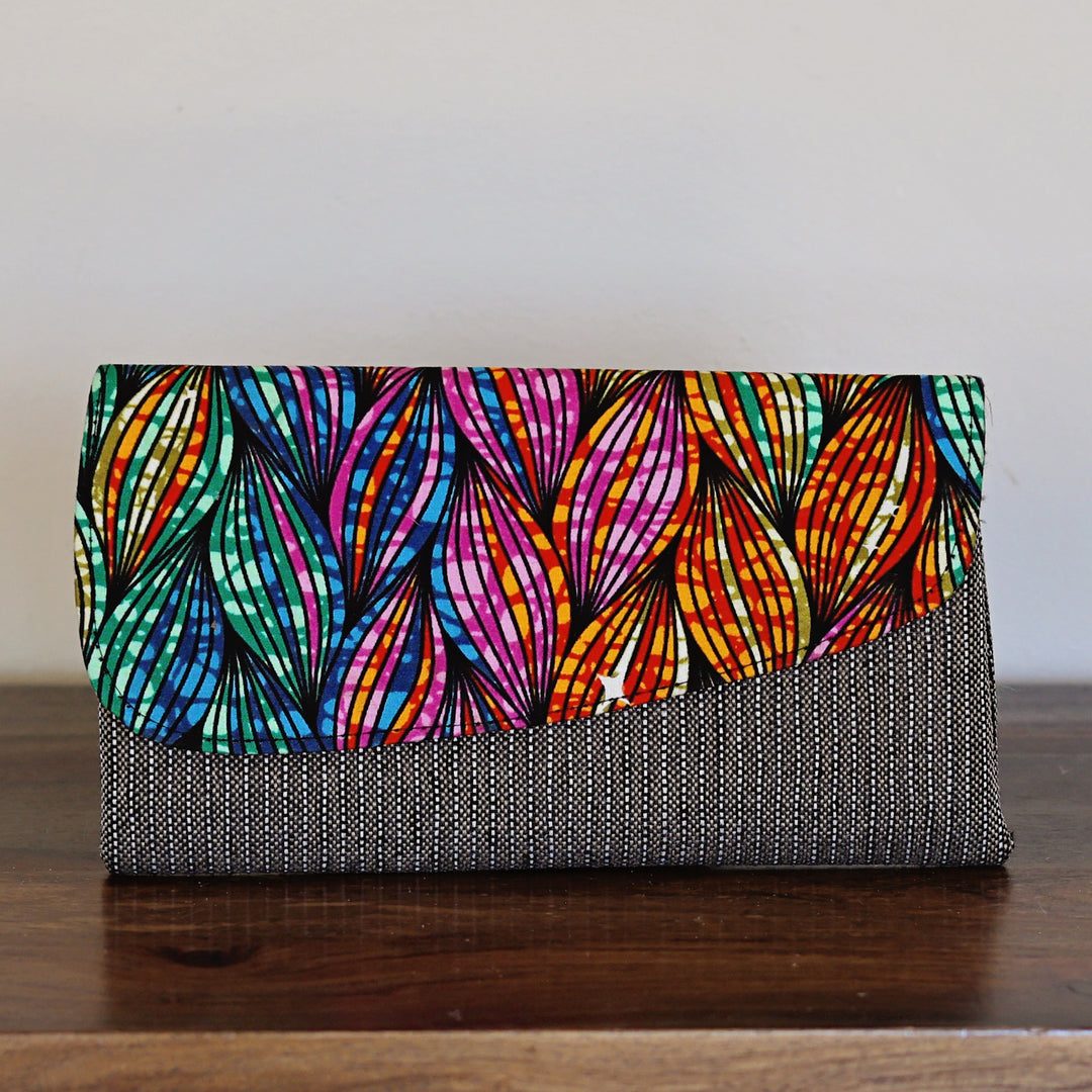 Clutch bag with colorful leaf-like batik pattern on a wooden surface.