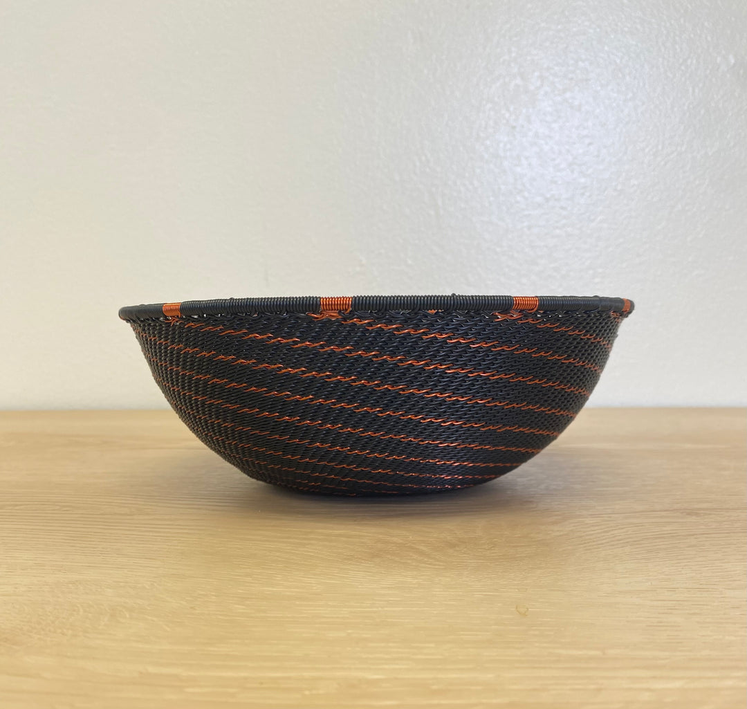 Bowl black Zulu wire wall basket with a bold handwoven copper spiral pattern.