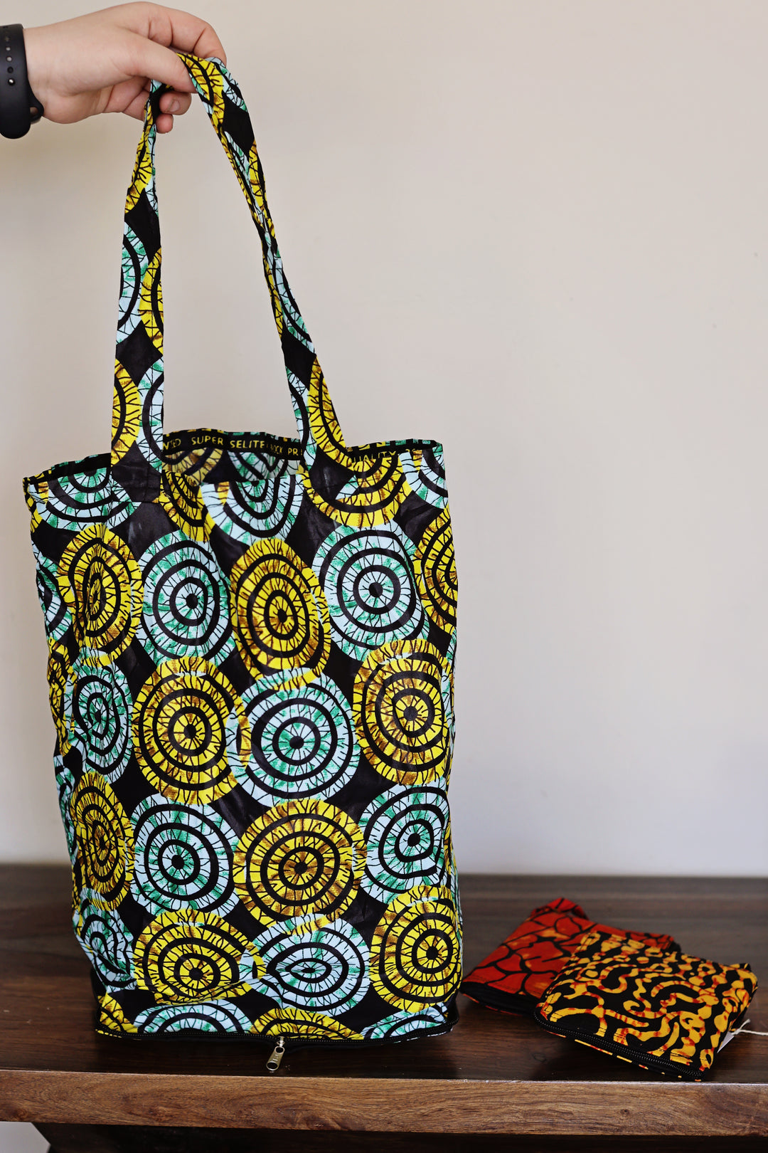 Tote bag with circular batik pattern held by a hand on a wooden surface.