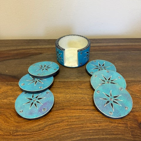 Set of six hand-carved soapstone coasters in assorted natural colors displayed in matching soapstone holder