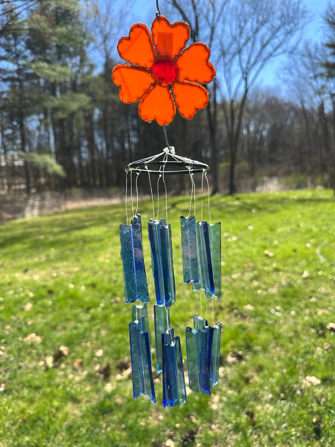 Decorative glass wind chime with an orange flower and blue glass rectangular pieces in a garden setting.