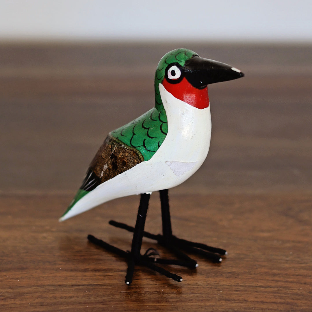 Colorful, hand-painted bird figurine on a wooden surface, made by artisans in Africa.
