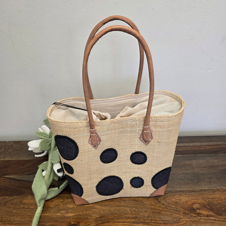 Handwoven Madagascar raffia tote showing sturdy leather handles, reinforced corners, and artisan weaving.