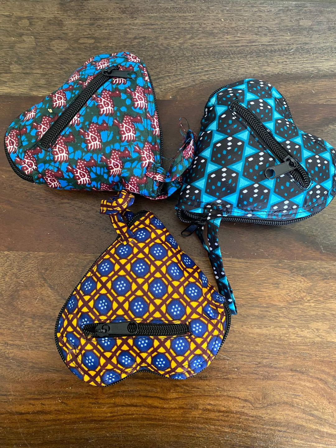 Three heart-shaped fabric reusable pouches with African patterns on a wooden surface.