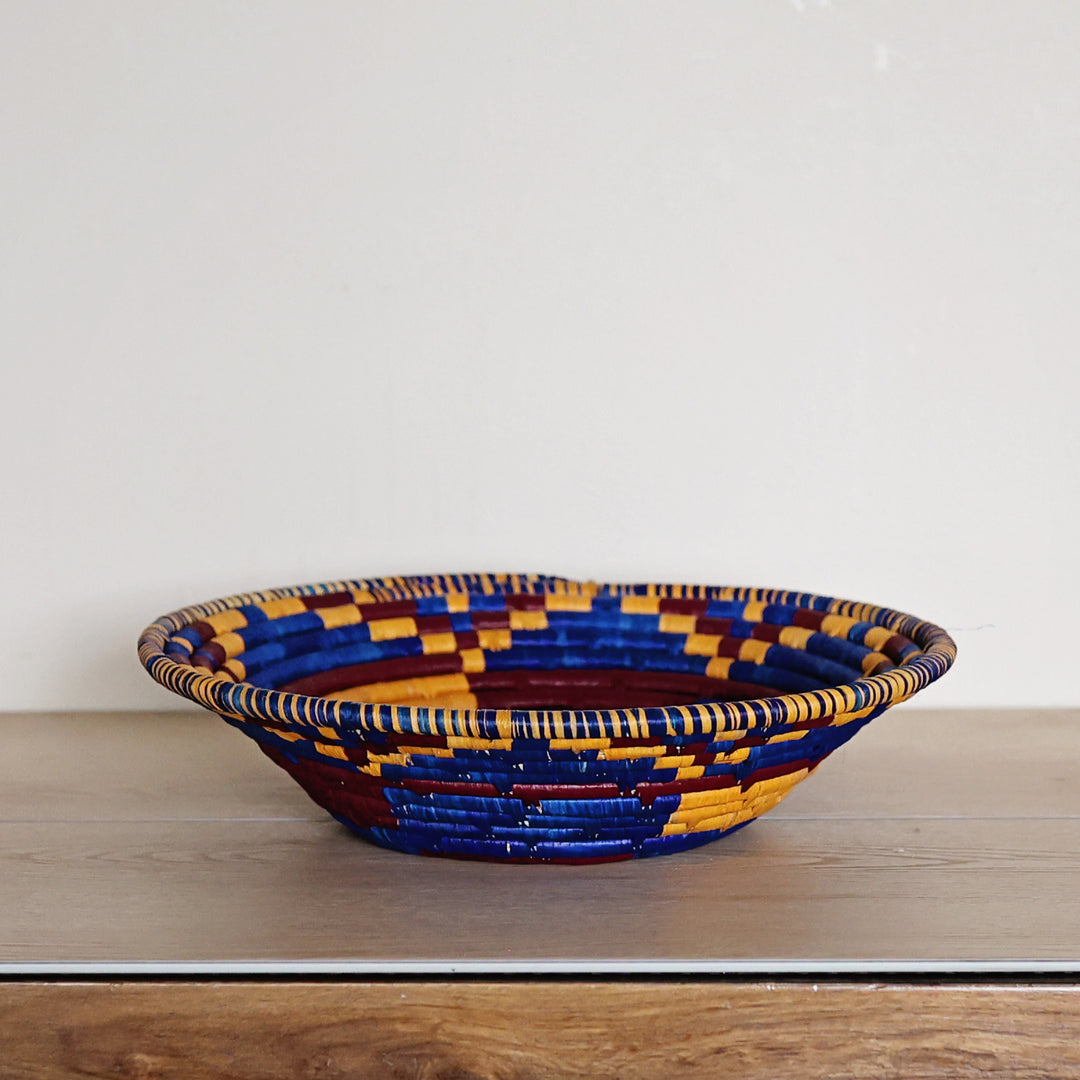 Side view of an Indigo Mosaic Bukedo and Raffia bowl handcrafted in Uganda from banana leaf stalks and palm raffia with rich indigo and gold woven details.
