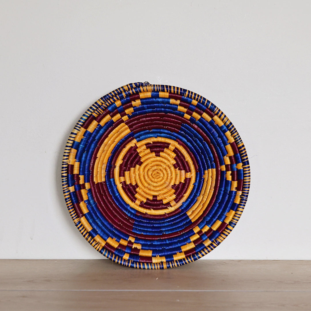 Handwoven Indigo Mosaic Bukedo and Raffia bowl handmade in Uganda featuring deep indigo, golden ochre, and burgundy woven patterns for fair trade home décor.